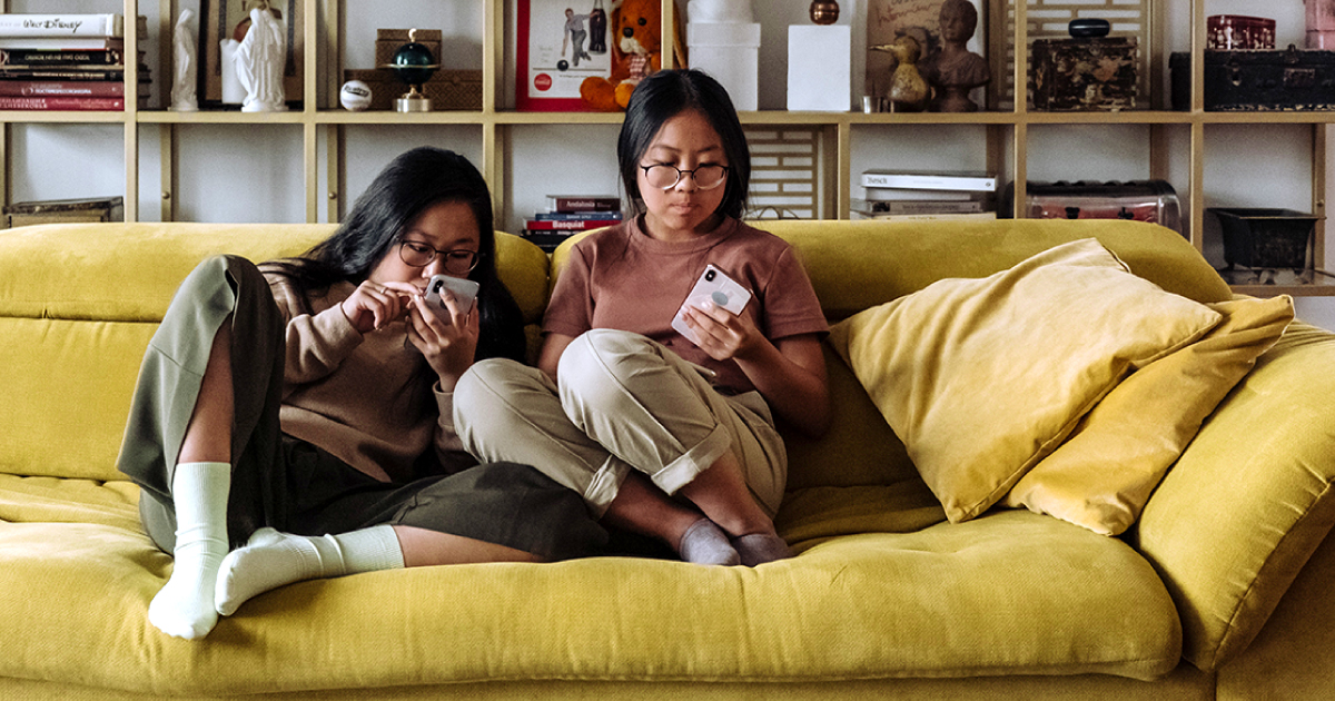 Two high school students sitting on a couch at home looking at their phones