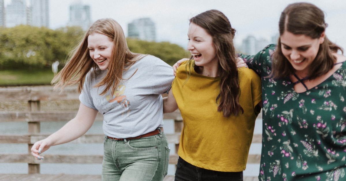 Three high school friends laughing and walking arm in arm