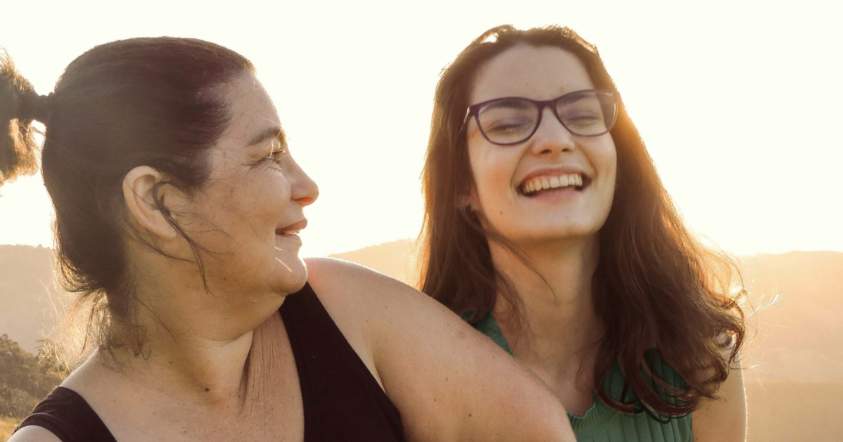 Mother and teenage daughter laughing together with the sun low in the sky